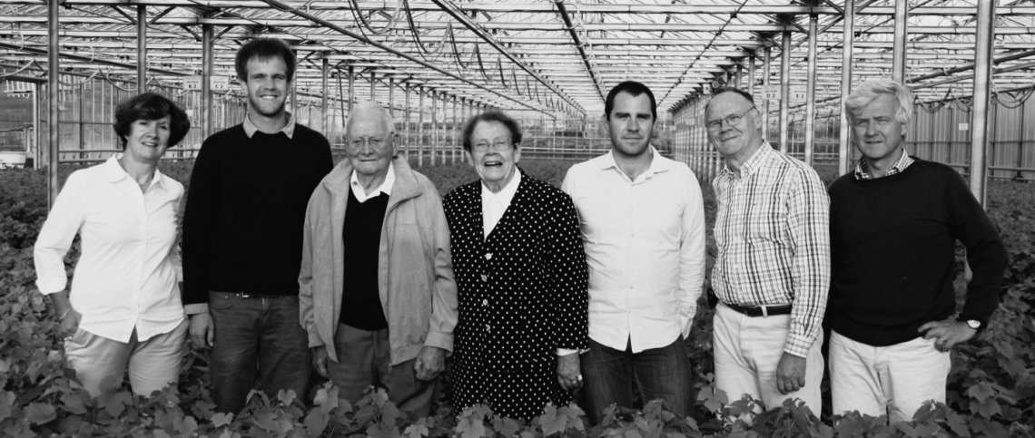 A group of people standing in a greenhouse, posing side by side among crops, in black and white.